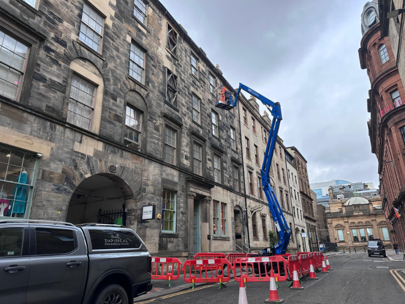 Blue cherry picker working on historic stone building with traffic barriers blocking the street