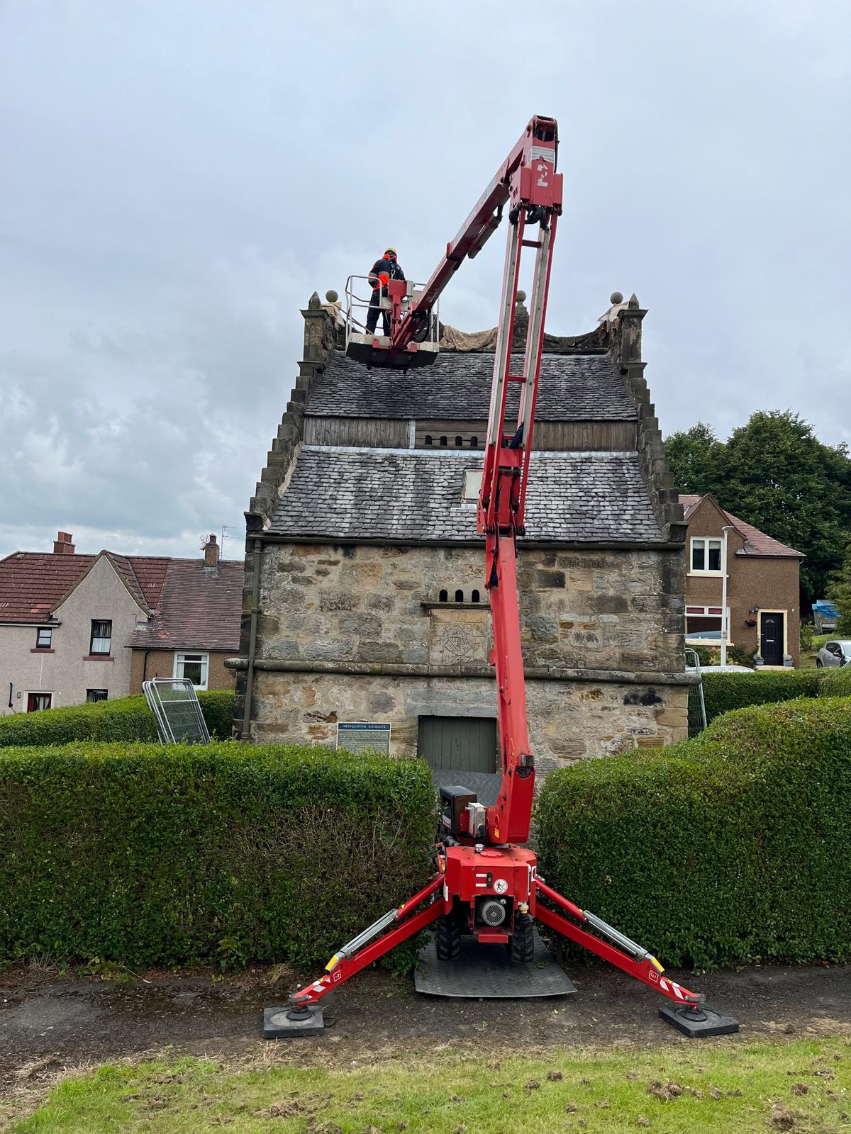 Red tracked spider lift with worker in basket performing roof repairs on historic stone building Red tracked spider lift with worker in basket performing roof repairs on historic stone building