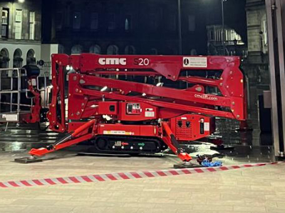 Red tracked spider crane set up indoors with safety tape barrier in warehouse or industrial space
