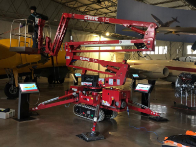 Red tracked spider crane positioned in aircraft hangar near yellow plane